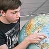Das Foto zeigt einen Studierenden der auf etwas auf einem Globus zeigt.