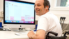 Auf dem bild sieht man Thorsten Lihl. Er sitzt am PC und lächelt jemanden außerhalb des Bildes an.