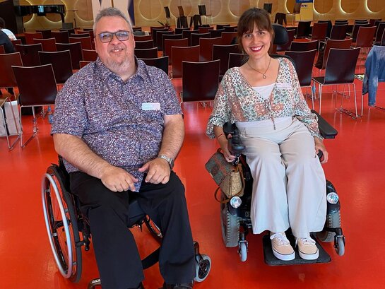 Bildungsfachkraft Helmuth Pflantzer und Landesbehindertenbeauftragte Nora Welsch auf der Abschlussveranstaltung des Projekts "Kurswechsel Kultur". Herr Pflantzer und Frau Welsch sitzen in ihren Rollstühlen und lächeln in die Kamera.