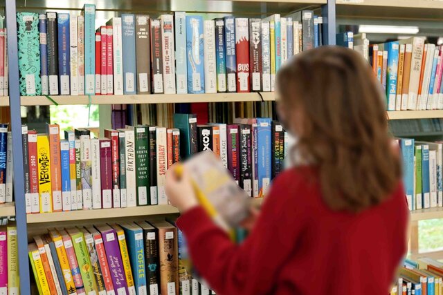 Eine Studentin steht vor einem Regal des Zentrums- für Kinder- und Jugendliteratur und nimmt sich ein Buch