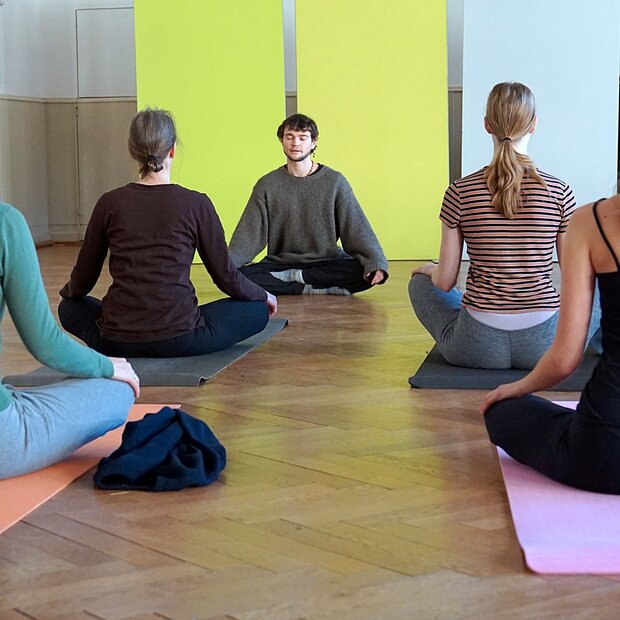 Yogalehrer und 4 Teilnehmerinnen sitzen im Schneidersitz auf Yogamatten