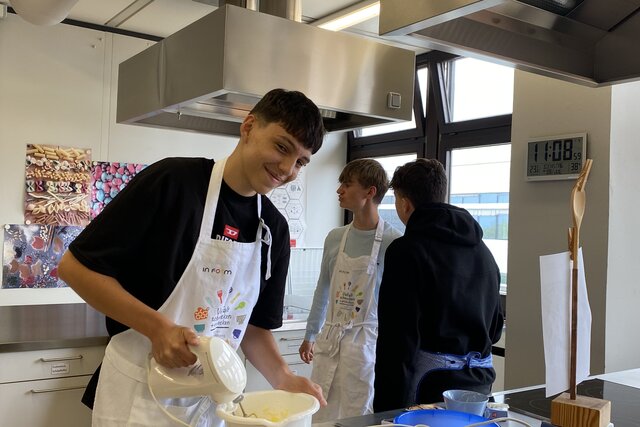Ein Student in der Lehrküche der Alltagskultur und Gesundheit im lernen über Ernährung und Gesundheitsthemen. Er hat ein Rührgerät in der Hand.
