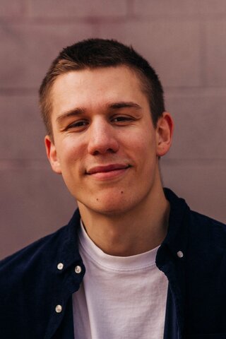 Zu sehen ist ein Portraitfoto von Alumnus Moritz Stock vor einer geziegelten Wand