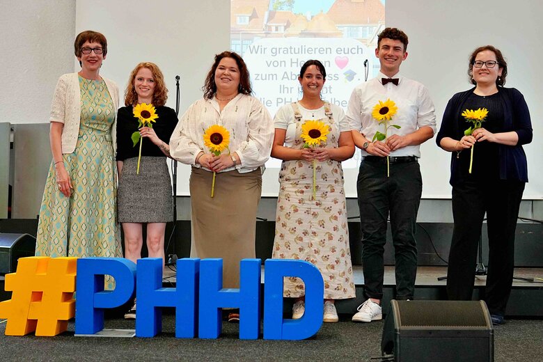 Zu sehen sind Rektorin Vach & Chiara Dold (ganz links, bzw. rechts) sowie 4 Absolvent:innen die für besonderes Engagement mit Sonnenblumen geehrt wurden.
