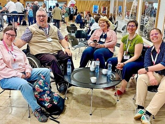 Das Foto zeigt verschiedene Personen um einen kleinen Tisch sitzend.