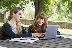 zwei Studierende an einem Tisch in der Natur während sie an einem Laptop arbeiten und daneben liegen Zettel und Stifte. Copyright Pädagogische Hochschule Heidelberg