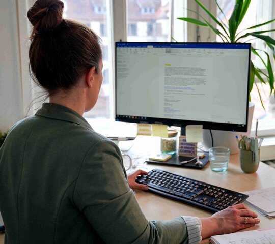 Eine Mitarbeiterin der Pädagogischen Hochschule Heidelberg steht an ihrem Stehtisch und arbeitet durch den Haltungswechsel gesund. 