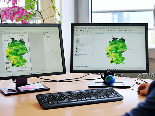 Bildschirme mit Deutschlandkarten, auf denen die Apfelblüte in farbigen Feldern erfasst ist: Gelbe Flächen  zeigen Regionen mit einem frühen Blütenbeginn, je dunkler das Grün, desto später kam die Apfelblüte. 