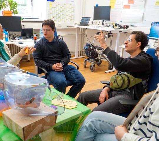 Das Bild zeigt einen Ausschnitt der Fortbildung. Vorne sind Modelle der weiblichen und männlichen Geschlechtsorgane auf einem Tisch, dahinter die Qualifizierungsteilnehmenden mit der Kursleiterin Kaya Schilling.