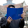 Auf dem Bild ist eine Person zu sehen, die den Jahresbericht der Hochschule liest. Sie steht im Innenhof der alten PH; ihr Gesicht ist nicht zu sehen. Der Fokus des Bildes liegt vielmehr auf dem Cover des Jahresberichts.