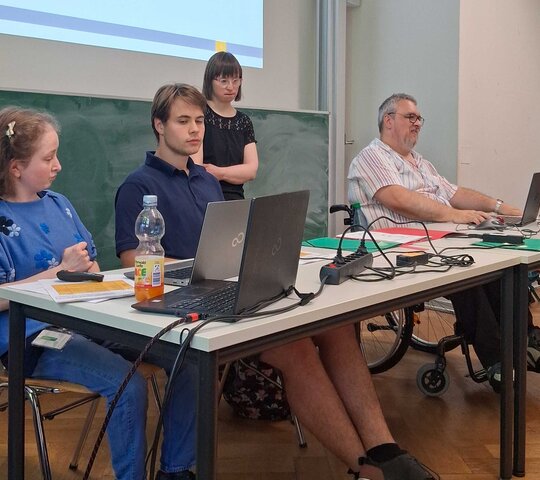 Das Bild zeigt Louisa Kabbe und Susann Bensch bei ihrer Modulprüfung. Sie sitzen bzw. stehen vor einer Tafel in einem Seminarraum der PH Heidelberg. Mit dabei auf dem Bild sind FSJ-Kraft Carl Hoffmann sowie Bildungsfachkraft Helmuth Pflantzer.