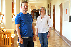 Die Porträtaufnahme zeigt links Johannes Hennies und rechts, etwas weiter hinten, Vera Heyl. Sie stehen im Altbauflur der Hochschule. Aufgrund der Corona-Pandemie halten sie Abstand. Copyright: PH Heidelberg