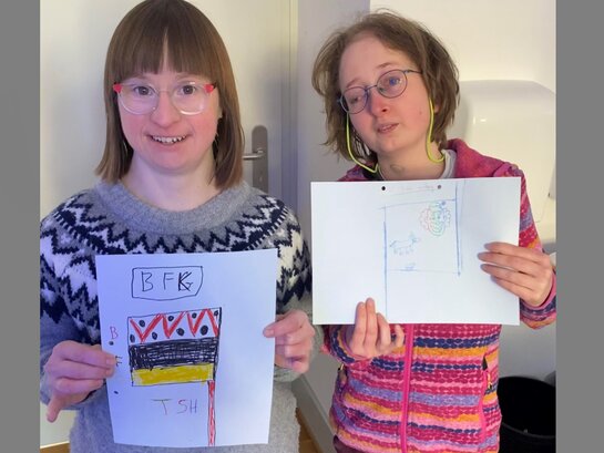 Susann Bensch und Louisa Kabbe präsentieren die Bildungsfachkräfte-Team-Flaggen, die im Rahmen eines Team-Building-Tags mit den schon fertig qualifizierten Bildungsfachkräften entstanden sind.