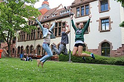 drei springende Menschen vor dem Altbau der Ph.