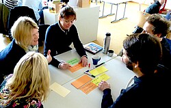  Lehrerinnen und Lehrer die sich an einem Tisch gegenüber sitzen.