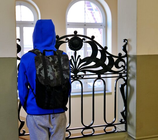 Zu sehen ist ein Junge von hinten an einem Geländer in einem Schulgebäude stehend