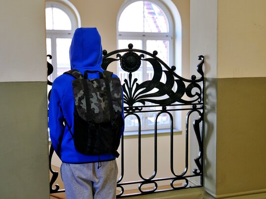 Zu sehen ist ein Junge von hinten an einem Geländer in einem Schulgebäude stehend