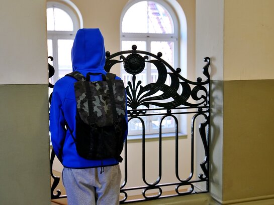 Zu sehen ist ein Junge von hinten an einem Geländer in einem Schulgebäude stehend