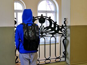 Zu sehen ist ein Junge von hinten an einem Geländer in einem Schulgebäude stehend