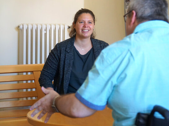 Das Bild zeigt Noemi Heister, die mit Helmuth Pflantzer spricht. Helmuth Pflantzer sitzt mit dem Rücken zum Betrachter in seinem Rollstuhl.