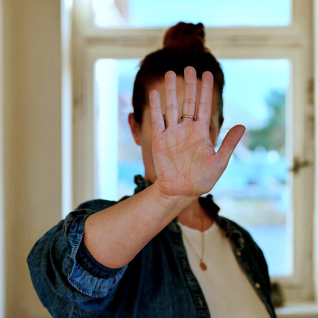 Zu sehen ist eine Frau, die sich ihre Hand abwehrend vors Gesicht hält