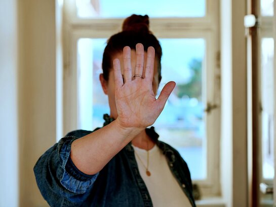 Zu sehen ist eine Frau, die sich ihre Hand abwehrend vors Gesicht hält