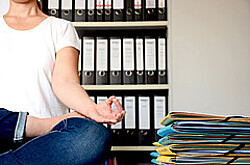 Person, die im Meditationssitz auf einem Bürotisch sitzt.