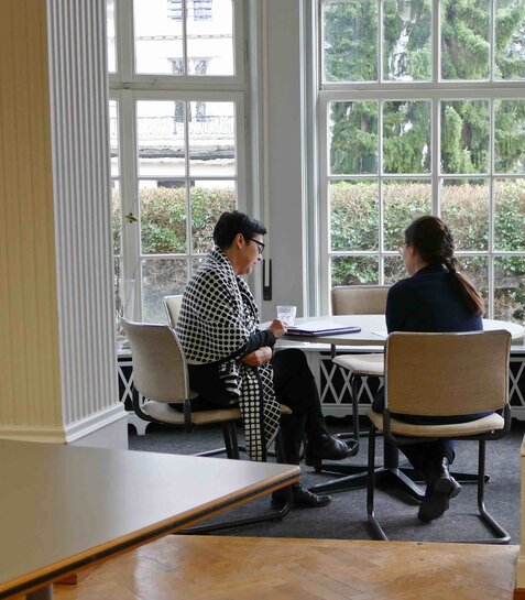 Zwei Personen sitzen an einem Tisch und befinden sich in einem Beratungsgespräch.