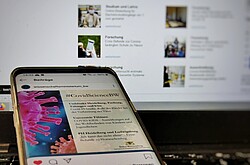 Das Bild zeigt ein Handy mit geöffneter Corona- Meldung vor einem Laptop.
