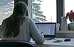 Das Foto zeigt eine Studierende im Homeoffice vor ihrem Laptop am schreiben.