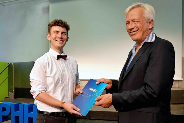 Zu sehen ist Prorektor Dammer (a.D.), wie er einem Alumnus den Bestehensbrief in einer PHHD-Mappe überreicht.
