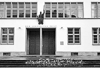 Gebäude der Universität Heidelberg. Über dem Tor steht "Dem lebendigen Geist". Vor dem Tor stehen Kerzen und liegen Blumen. Es ist ein schwarz-weiß Foto.