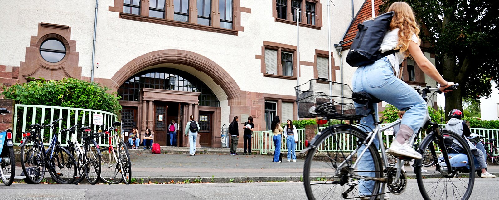 Eine Studentin des Lehramts fähr auf dem Fahrrad an der Pädagogischen Hochschule Heidelberg vorbei. Zu sehen ist der Altbau in dem Leitungsgremien und zentralen Einrichtungen sind.