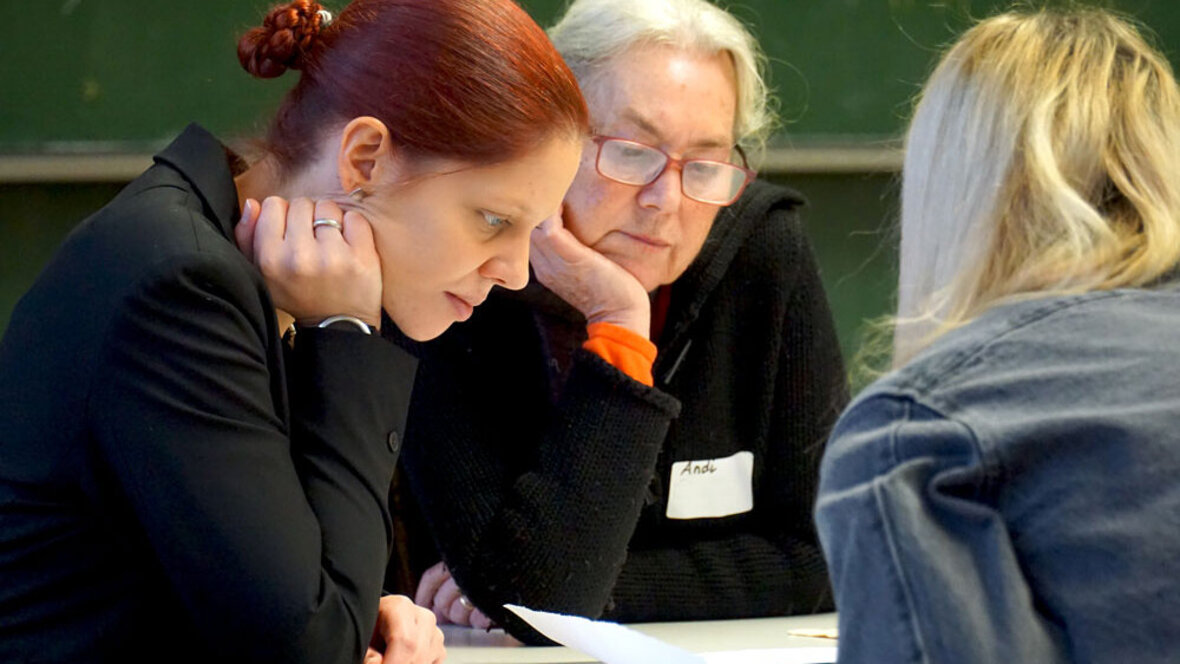 Zwei Frauen schauen konzentriert auf Papiere, die vor ihnen auf dem Tisch liegen.