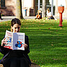 Frau sitzt im Innenhof der Hochschule und liest die aktuelle daktylos-Ausgabe. Im Hintergrund laufen Personen bzw. sitzen auf dem Gras.