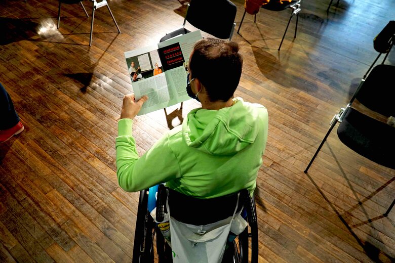 Das Foto zeigt einen Mann von hinten. Er sitzt im Rollstuhl und liest eine Ausgabe des daktylos Magazin.