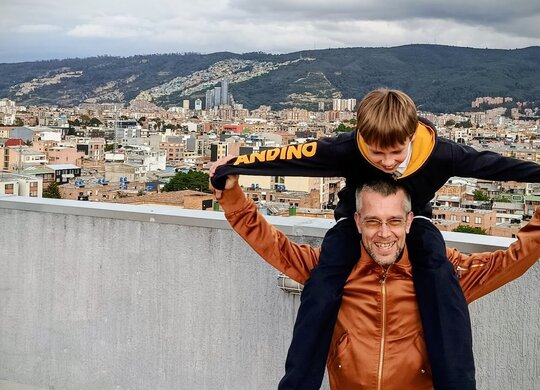 Zu sehen ist der Sonderpädagogikstudent Julian mit seinem Sohn Lucas auf den Schultern vor der Metropole Bogota