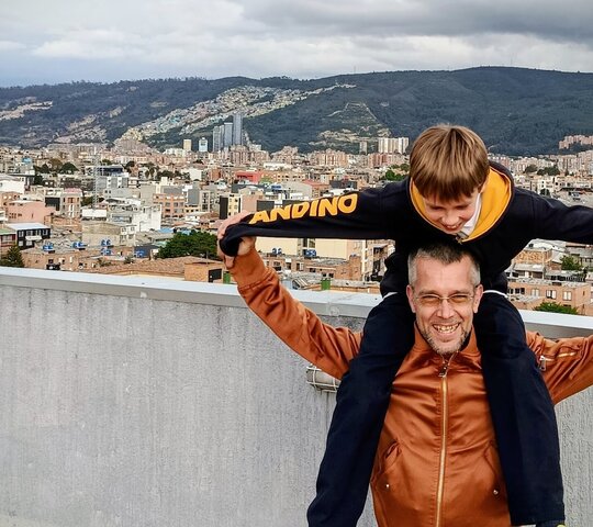 Zu sehen ist der Sonderpädagogikstudent Julian mit seinem Sohn Lucas auf den Schultern vor der Metropole Bogota