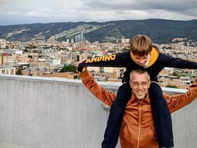 Zu sehen ist der Sonderpädagogikstudent Julian mit seinem Sohn Lucas auf den Schultern vor der Metropole Bogota