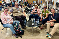 Das Bild zeigt eine Gruppe von Teammitgliedern des AW-ZIB auf der Tagung in der Schweiz. Vier Frauen und ein Mannim Rollstuhl sitzen um einen niedrigen Tisch herum und lächeln in die Kamera.