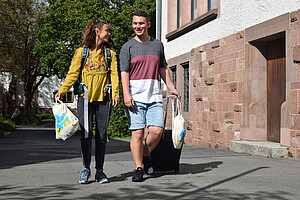 Das Foto zeigt zwei Studierenden, die mit Auslandgepäck die Hochschule verlassen.