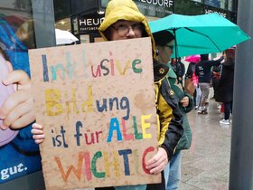 Bildungsfachkraft Thilo Krahnke auf der Kundgebung in Stuttgart. Er trägt ein selbst gestaltetes Plakat vor sich. Auf dem Plakat steht in bunten Buchstaben: Inklusive Bildung ist für alle wichtig.