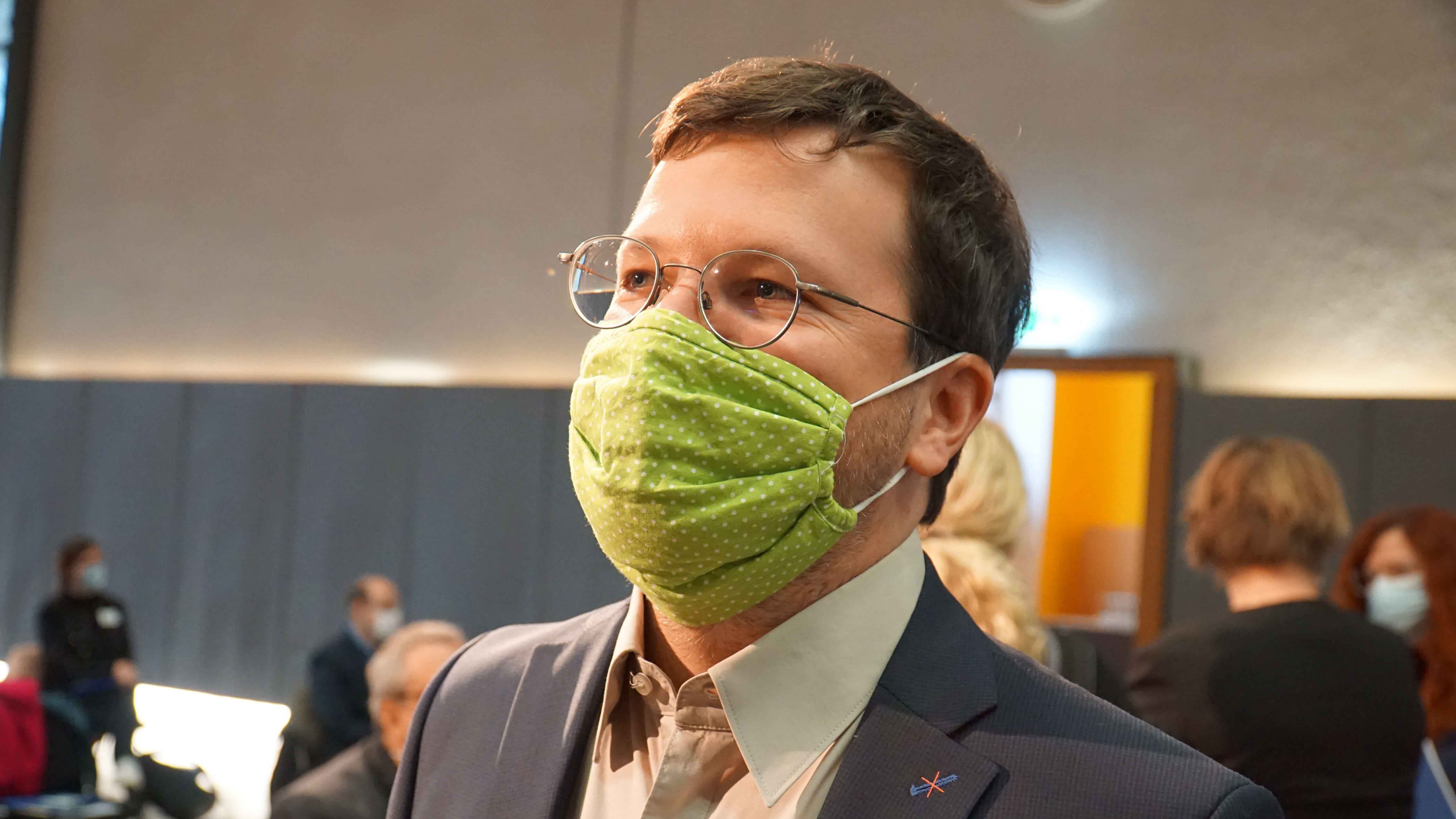 Seitenaufnahme eines Mannes mit grünem Mund-Nasen-Schutz.