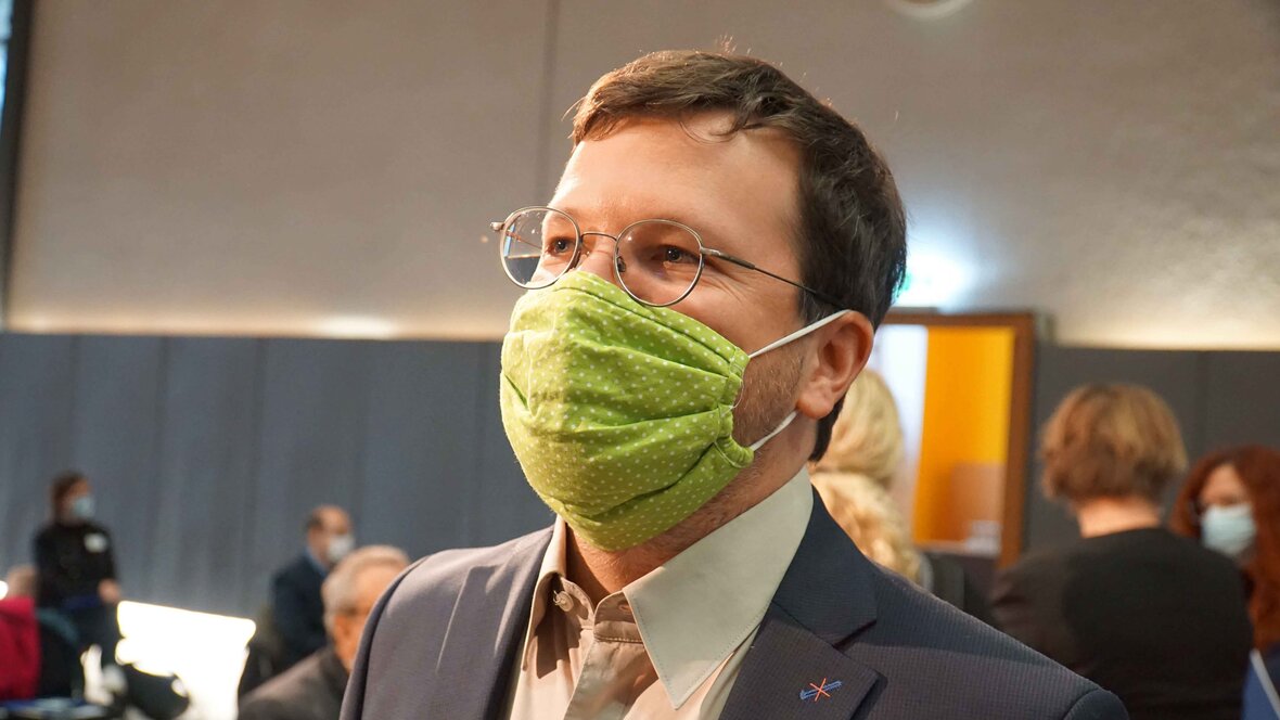 Seitenaufnahme eines Mannes mit grünem Mund-Nasen-Schutz.