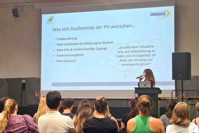 Eine Studentin steht auf der Bühne und präsentiert die Forschungsergebnisse ihres Seminars. Dies verdeutlicht die Forschende Lehre, die an der Pädagogischen Hochschule Heidelberg praktiziert wird.