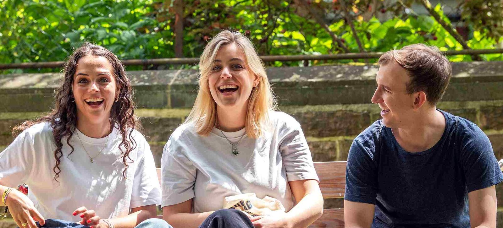 Zwei Studentinnen und ein Student sitzen in der Hängeschaukel. Alle drei lachen deutlich. Im Hintergrund sieht man den Innenhof der Hochschule.