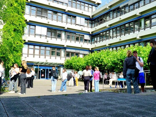 Studierende stehen in kleinen Gruppen vor dem Neubau und unterhalten sich.