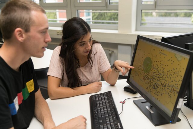 Zwei Personen vor einem Bildschirm auf dem GEographische Daten zu sehen sind