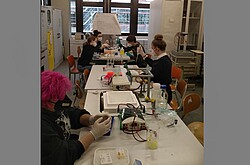 Das Bild zeigt mehrere Personen an mehrenen Tischen sitzen. Auf den Tischen liegen verschiedene Experimente. Copyright Valentin Kleinpeter