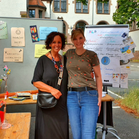 Frau Przewalla und Frau Müller stehen vor dem Infostand der NLS-Koordination